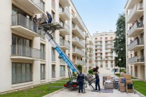 Équipe déménageant des meubles par monte-charge extérieur sur un immeuble, avec plates-formes et chariot élévateur, dans une cour pavée. comment déménager en situation de handicap intégré.
