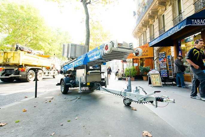 Chariot élévateur et camion de déménagement garés sur une rue urbaine avec des élèves et des magasins en arrière-plan.
